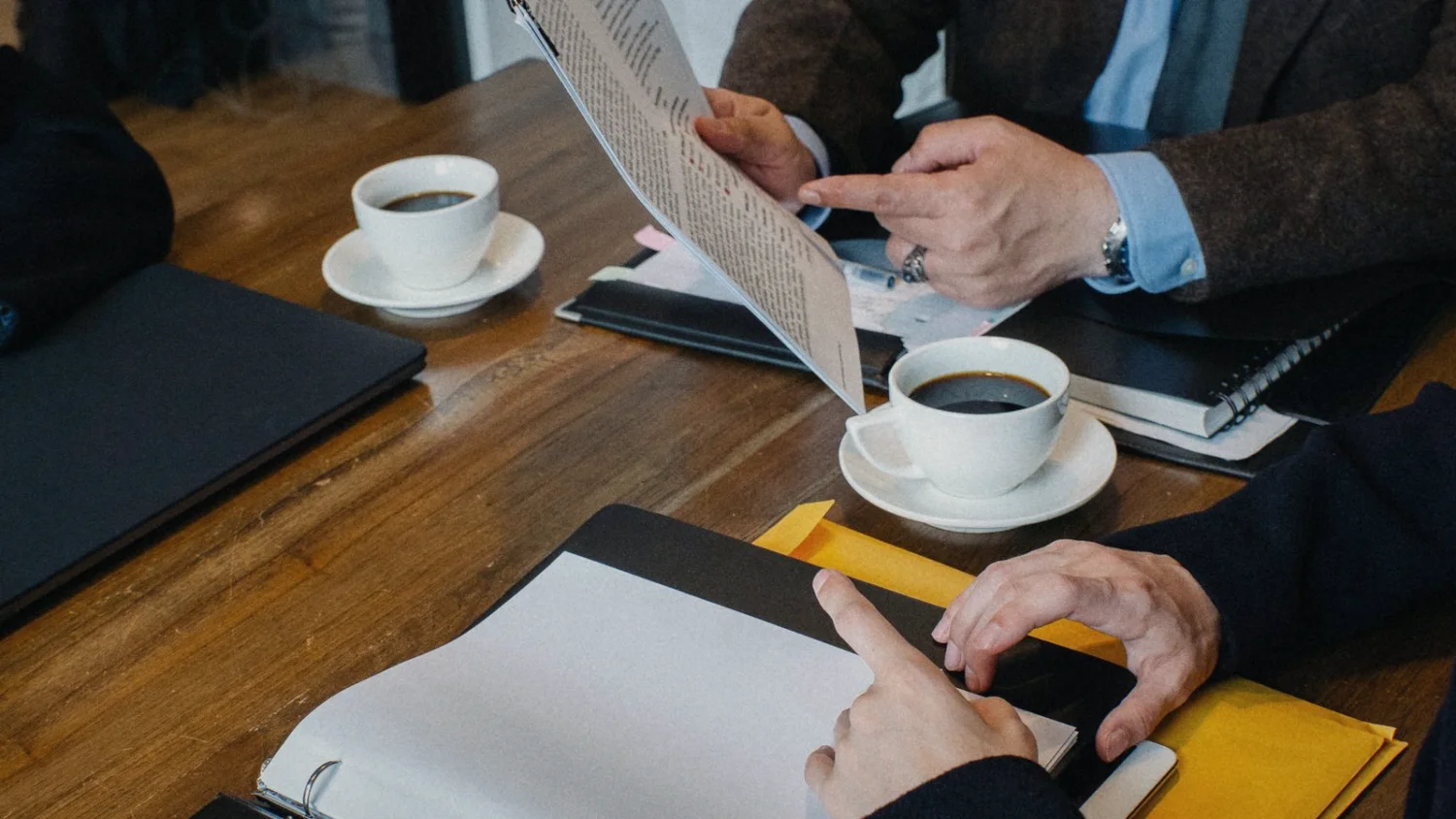 The same table: a hand pointing at a printed page, beside coffee and an open binder